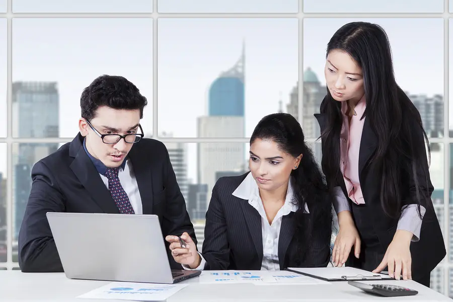 Internationales Team aus drei Kolleginnen und Kollegen arbeitet gemeinsam am Laptop – interkulturelles Training für Unternehmen